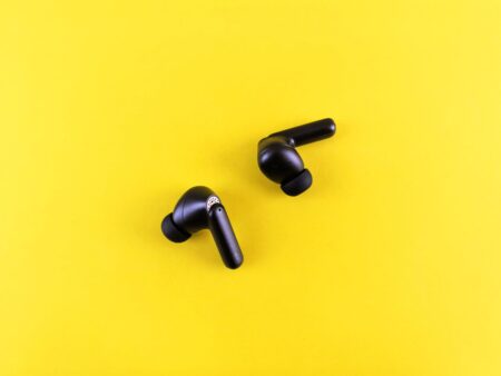 A pair of white wireless earbuds resting on a surface near their charging case