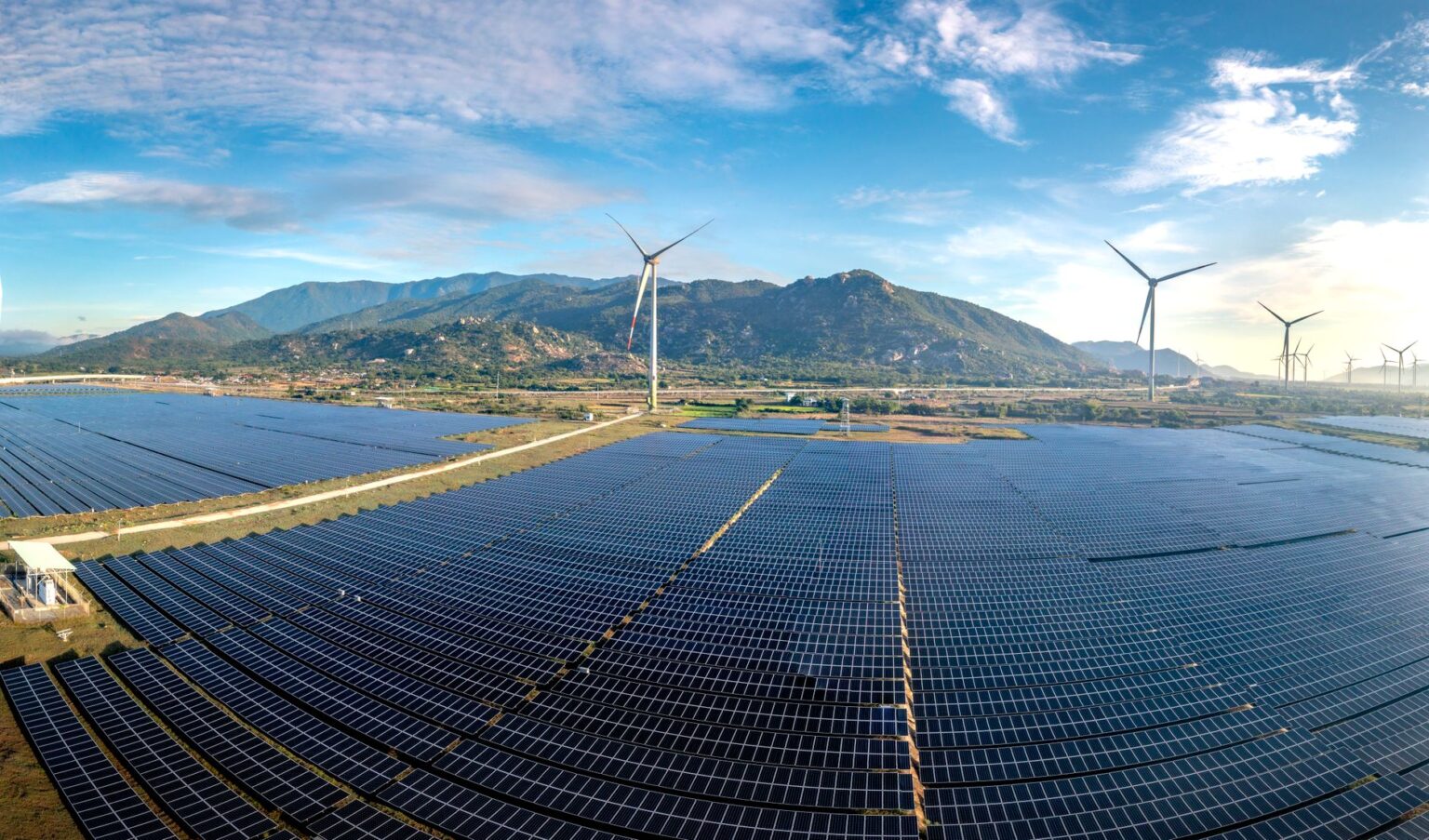 Aerial view of a large utility-scale solar farm with rows of panels under a blue sky