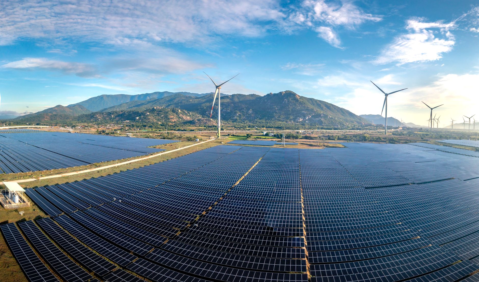 Aerial view of a large utility-scale solar farm with rows of panels under a blue sky