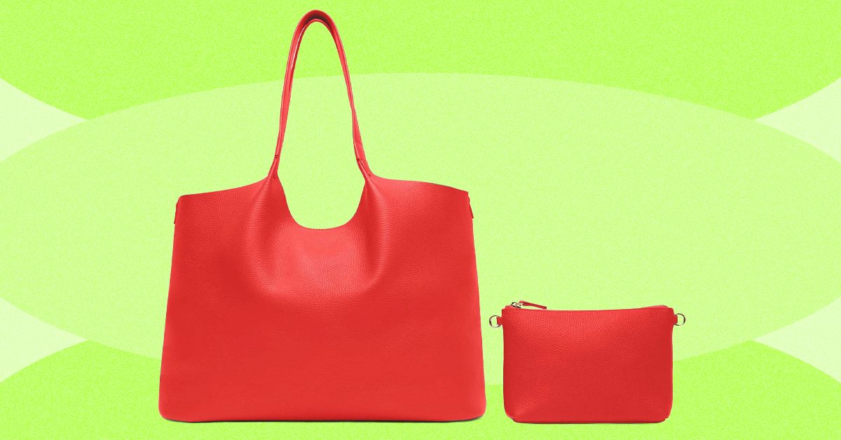 A structured full-grain leather tote bag on a wooden desk beside a laptop